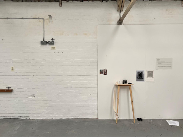 view of installation including a brownie camera on a stand with drawings, photographs and small sculptures on a white brick wall